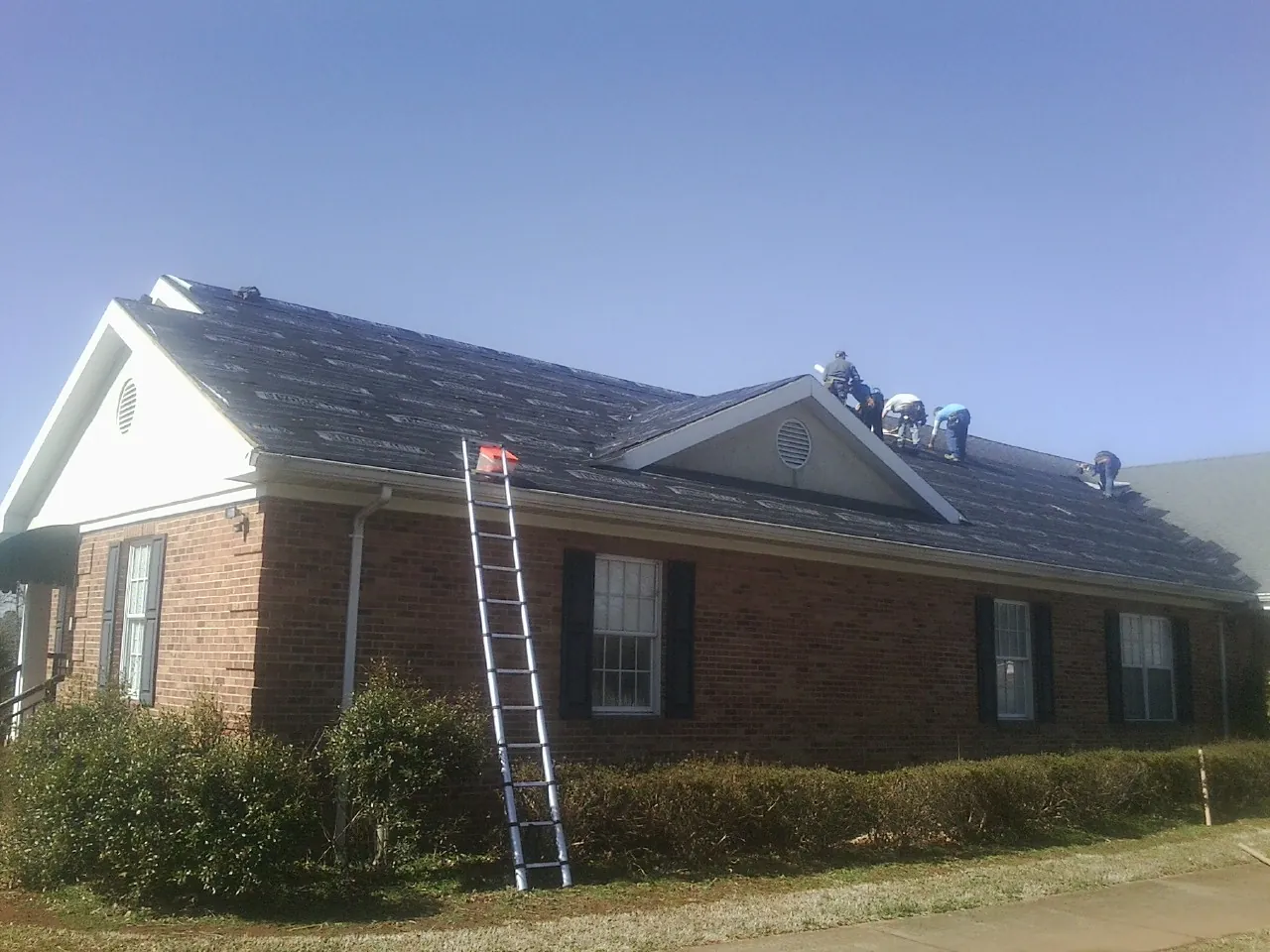Crew tearing shingles off a brick ranch roof with a ladder set — Emergency Roof Repair work by our crew in Farmville