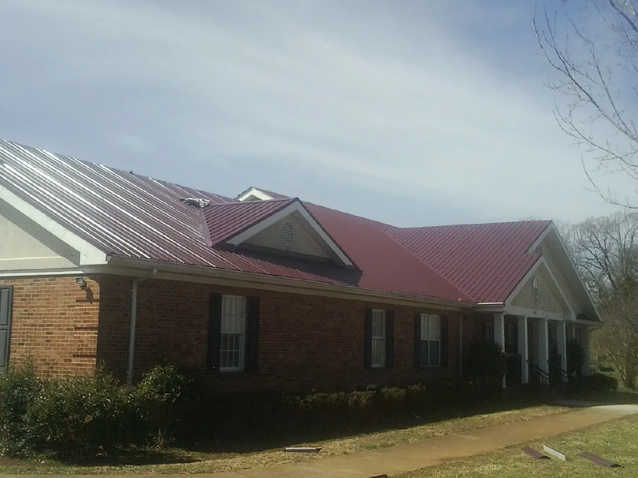 Red metal roof with gabled entries on a long brick building, from a Hail Damage Roof Repair job in Farmville
