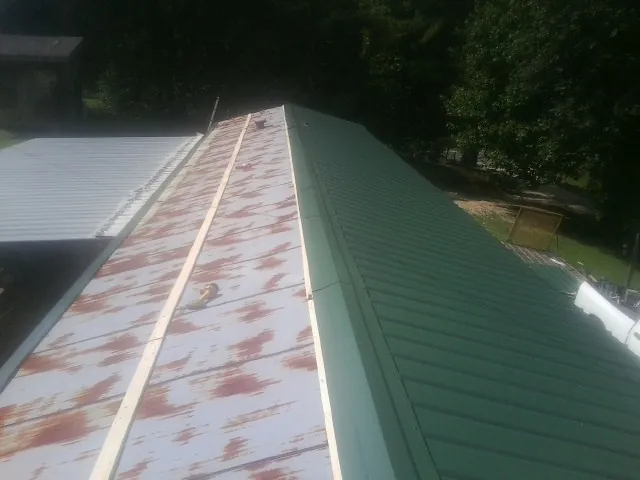 Old rusted panels beside newly installed green metal roofing — Wind Damage Roof Repair by Roofing Brothers in Farmville