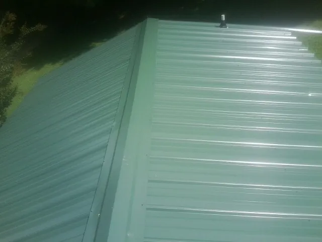 New green metal panels meeting at the ridge of a roof — Flat Roof Repair work by our crew in Farmville