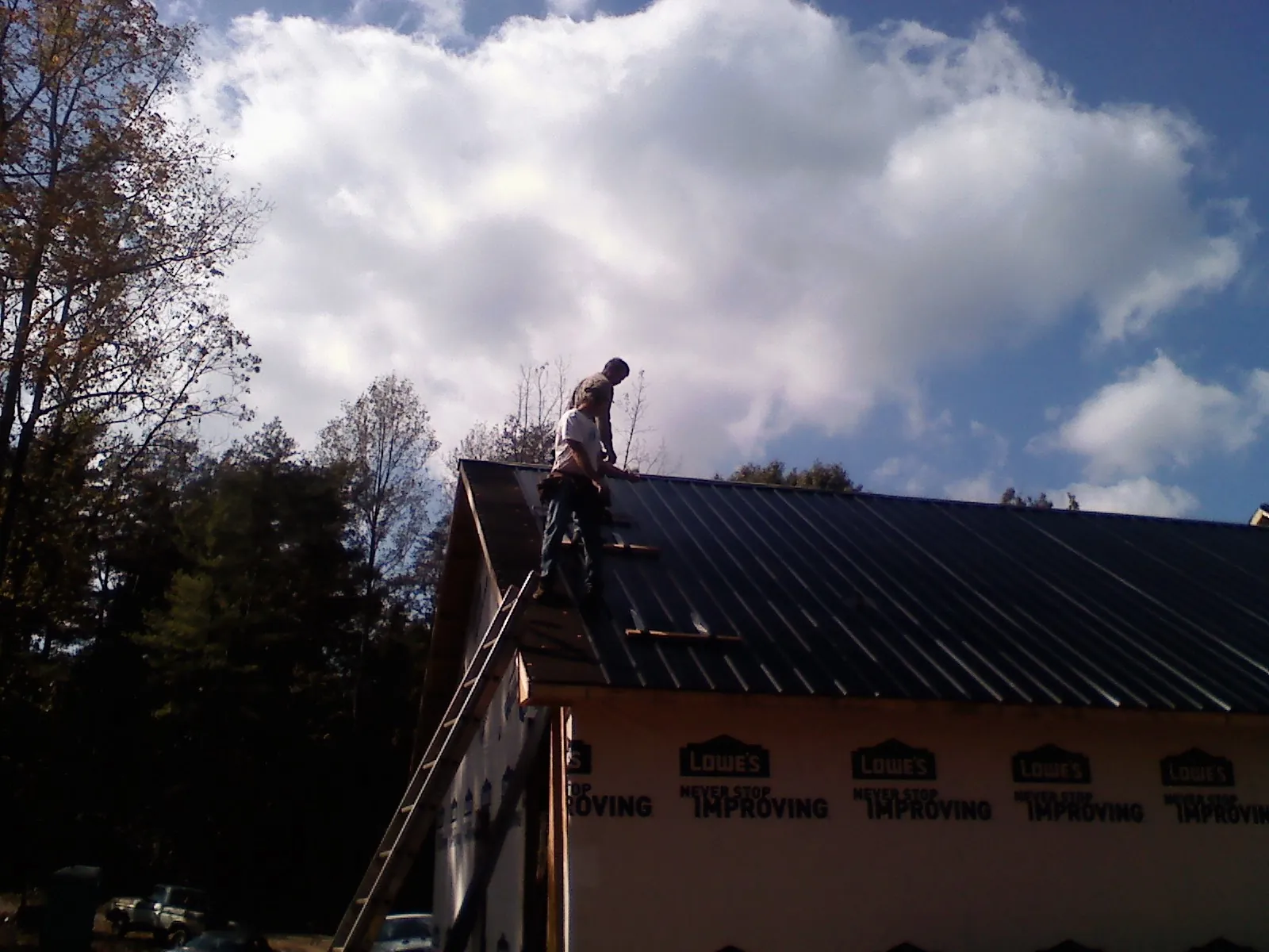 Roofer fastening dark metal panels high against a cloudy sky, from a Roof Inspection job in Farmville