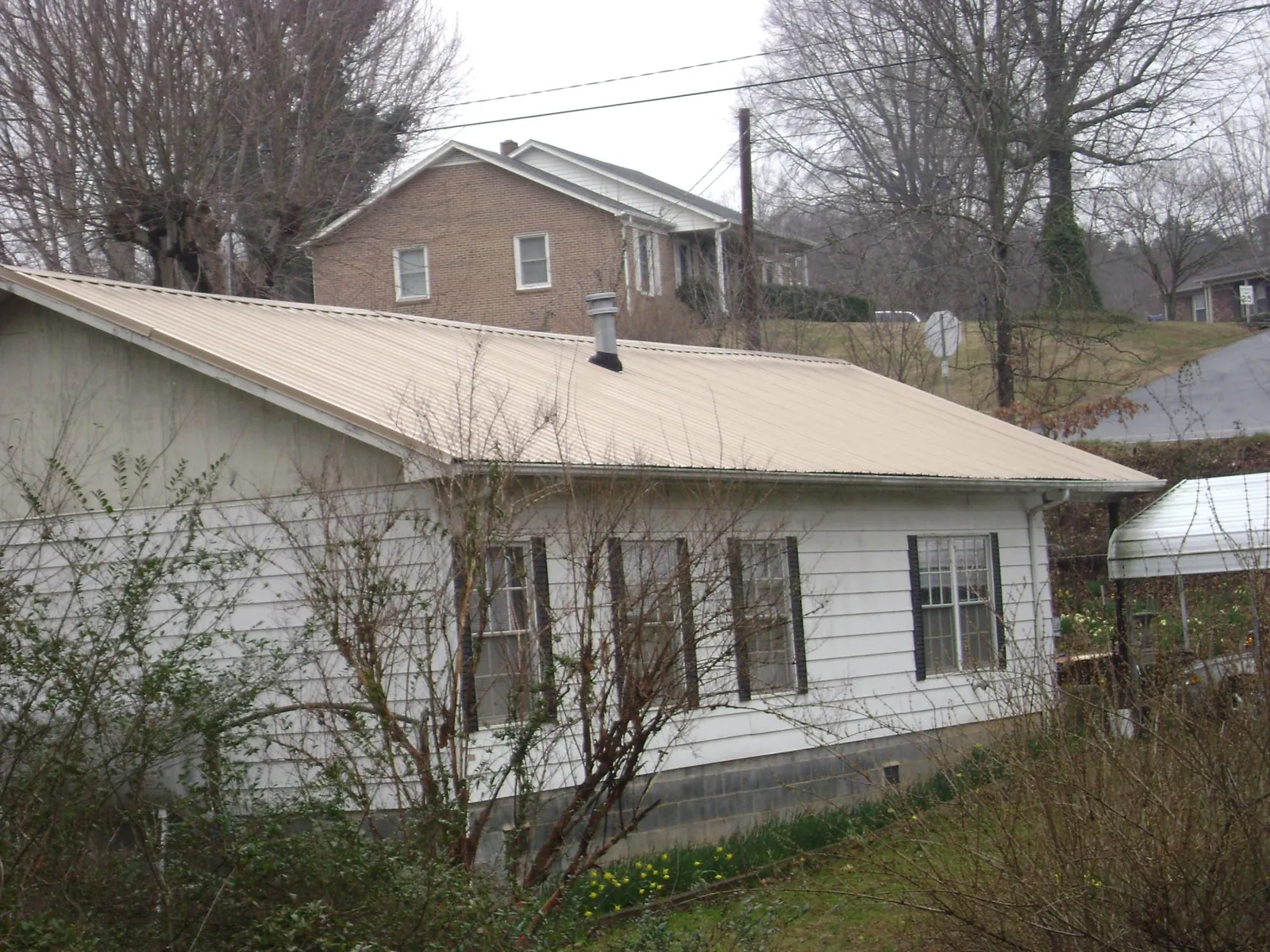 Tan metal roof on a white sided house set into a hillside — Commercial Roofing by Roofing Brothers in Farmville