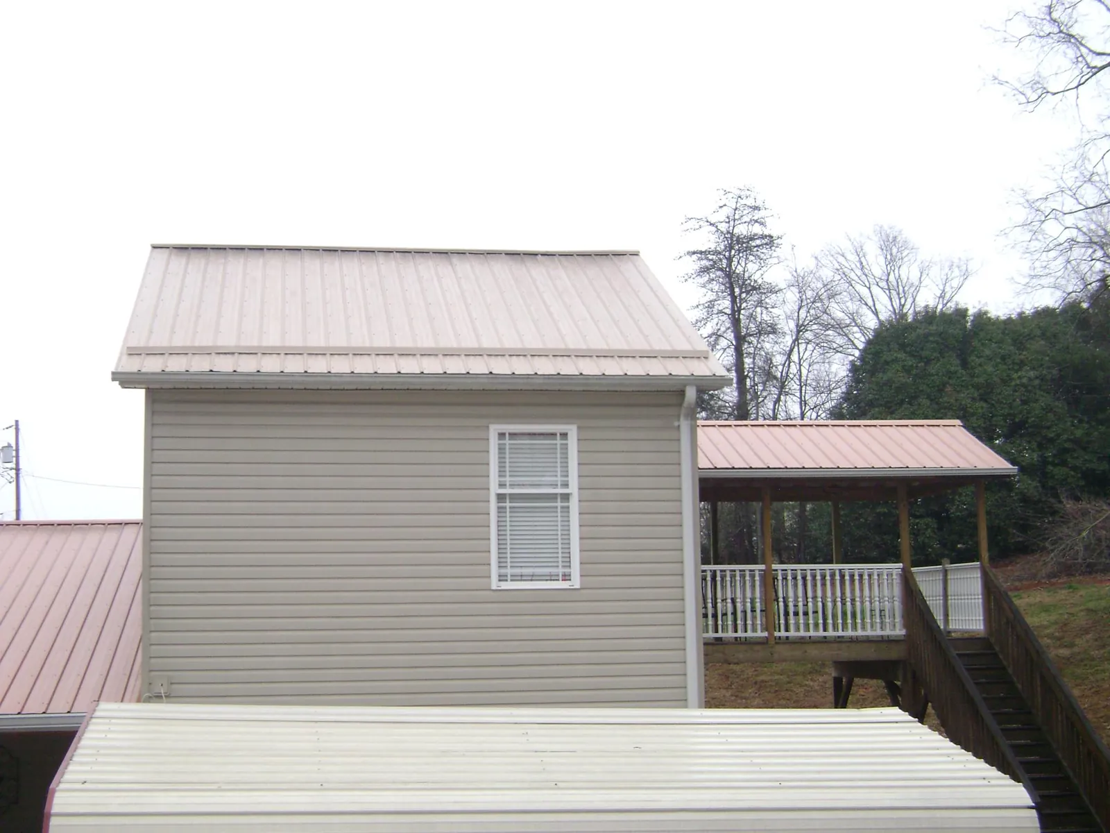 Tan metal roofs on a two story addition and attached porch, from a Roof Replacement job in Farmville