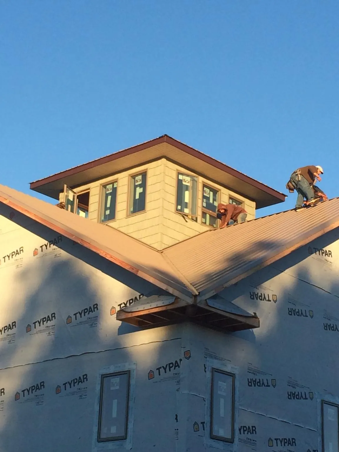 Roofers working around a rooftop cupola on a new metal roof at sunset — Roof Waterproofing in Farmville by Roofing Brothers